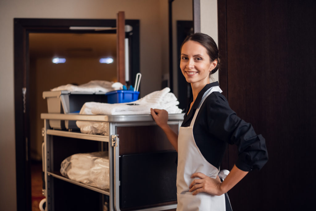 Smiling hotel maid with fresh towels doing housekeeping.